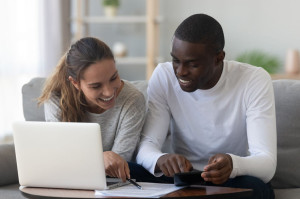 Happy smiling mixed race couple calculating domestic bills at home